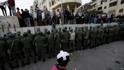 Demonstrators and security forces line concrete barrier