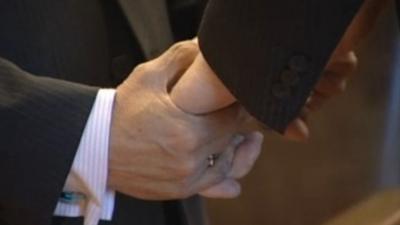 Two men hold hands at a civil ceremony