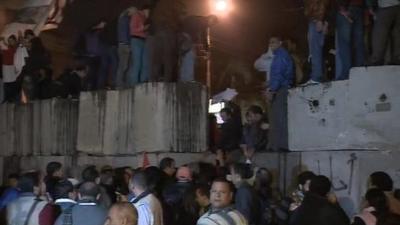 Protesters climb through gap in wall