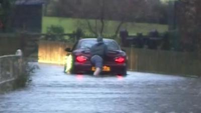 A man pushing his car through flood water