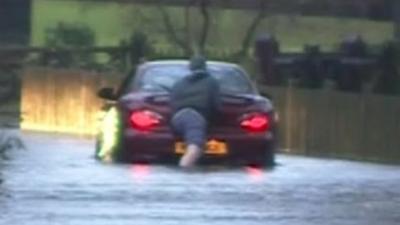 A man pushing his car through flood water