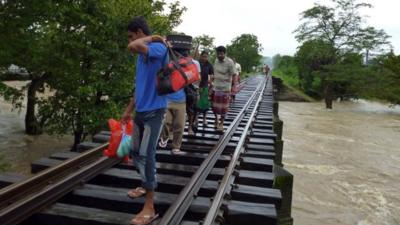 Sri Lankans walk on a rail road bridge across rising floodwaters