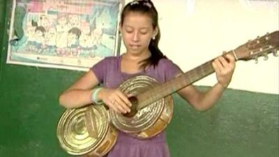 Girl plays guitar made of old cans