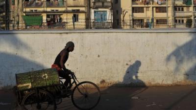 A Burmese worker uses a tricycle to transport an oil drum