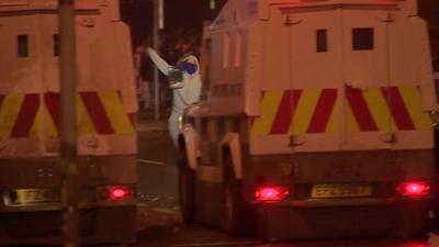 Man in hooded top and face covering throws missile at police vans