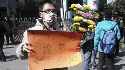 A man wearing a mask with the word 'Silent' holds a banner reading: 'Let"s chase our dreams together, go Southern Weekly newspaper' during a protest outside the headquarters of the newspaper in Guangzhou, Guangdong province