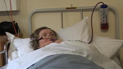 Patient in hospital bed drinking from a long straw out of a water bottle