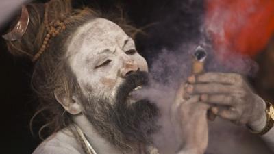 A Sadhu smokes marijuana on the banks of river Ganges