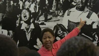 Antoinette Sithole shows a group of schoolchildren a picture of herself as a schoolgirl, screaming after her brother was shot and killed by the police in June 1976