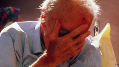 elderly man covering his face