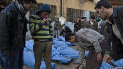 Men look for their relatives amongst the bodies of Syrian civilians executed and dumped in the Quweiq river