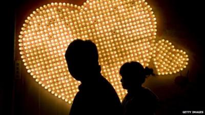 A couple walk at night past some lights in the shape of hearts