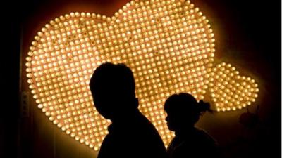 A couple walk at night past some lights in the shape of hearts