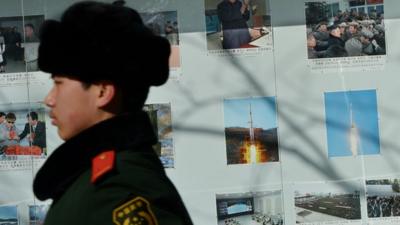 A Chinese policeman marches past photos of North Korea's recent rocket launch outside the North Korean embassy in Beijing