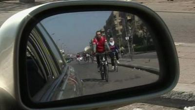 A cyclist seen in the side mirror of a car