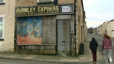 Children walking past a boarded up shop in Burnley