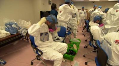 Fukushima clear-up workers putting on protective clothing before a visit to a contaminated area at the plant