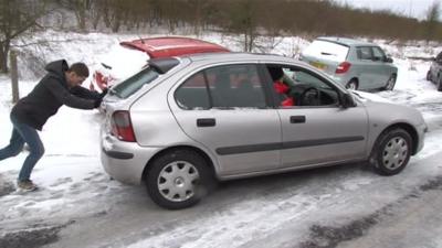 Man pushing car on snowy road