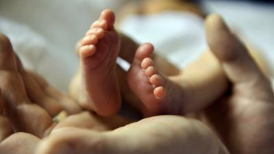 A father cradles the tiny feet of his five-day-old baby girl