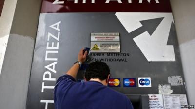 A man standing next to an ATM outside a branch of Laiki Bank in Nicosia