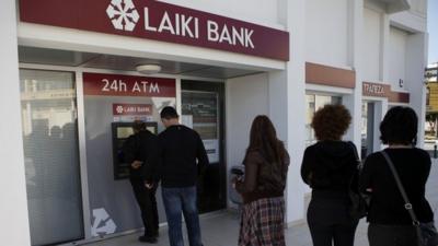 People queue to use an ATM machine outside of a Laiki Bank branch in Larnaca, Cyprus