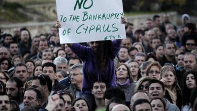 Woman sitting on shoulders of protester, holding sign saying "No to the bankruptcy of Cyprus"