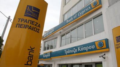 A Bank of Cyprus branch with a Piraeus Bank logo seen in foreground, in Athens