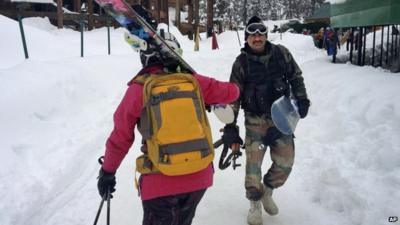 Indian Army soldier carries a snowboard and an automatic rifle as he walks past a skier below the gondola at Gulmarg, Kashmir