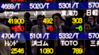 Pedestrians are reflected on a share prices board in Tokyo