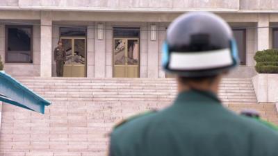 A South Korean soldier and his North Korean counterpart look at each other across the border