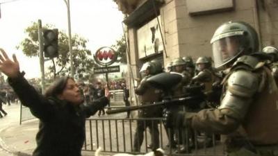 Police holds gun as protester stands in front