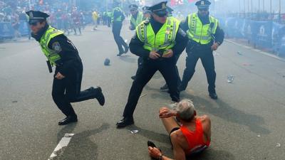 Bill Iffrig, 78, lies on the ground as police officers react to a second explosion at the finish line of the Boston Marathon