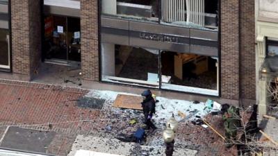 A man in a bomb-disposal suit investigates the explosion site