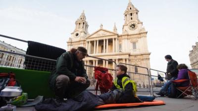 Spectators sitting behind barrier outside St Paul's