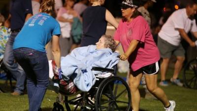 An elderly person is assisted at a staging area at a local school stadium following an explosion at a fertilizer plant