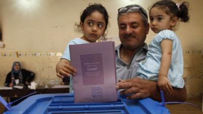 An Iraqi man, holding his two daughters, casts his ballot at a polling station in Basra, Iraq,