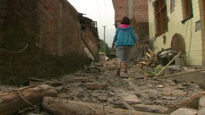 A woman walks through rubble in the village of Longmen
