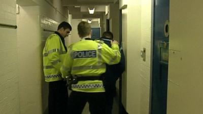 Police officers with young person in corridor leading to cells