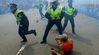 Police officers react to a second explosion at the finish line of the Boston Marathon