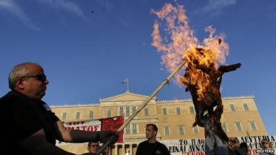 Protesters burn an effigy depicting a Greek worker during a rally against the government’s austerity reform program in Athens