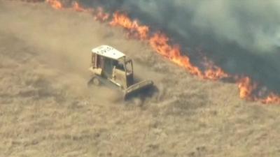 A vehicle drives along a field next to a line of wildfire