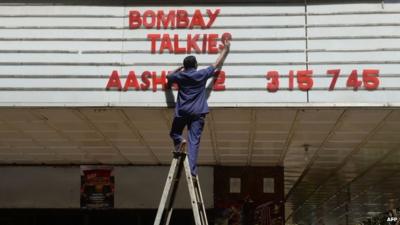 An employee of the New Excelsior Theatre puts up letters spelling out the movie "Bombay Talkies" in Mumbai