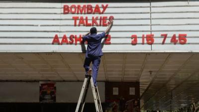 An employee of the New Excelsior Theatre puts up letters spelling out the movie "Bombay Talkies" in Mumbai