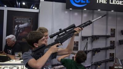 A teenager takes aim with a gun made by Colt at a booth during the National Rifle Association's annual meeting in Houston, Texas.