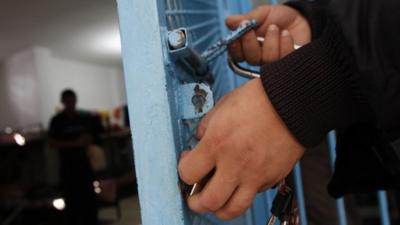 A prison guard closes the gate of a cell