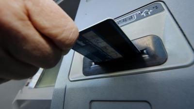 A person inserts a debit card into an ATM machine