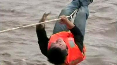 A man hangs on a rope above the flood water