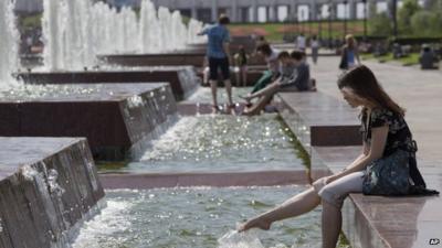 People sit at a fountain in a park in Moscow, Russia