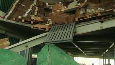 Stacks of boxes and a pallet hanging over the edge of a broken upper floor