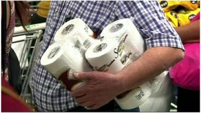 A man carrying two packs of toilet paper in a supermarket in Caracas